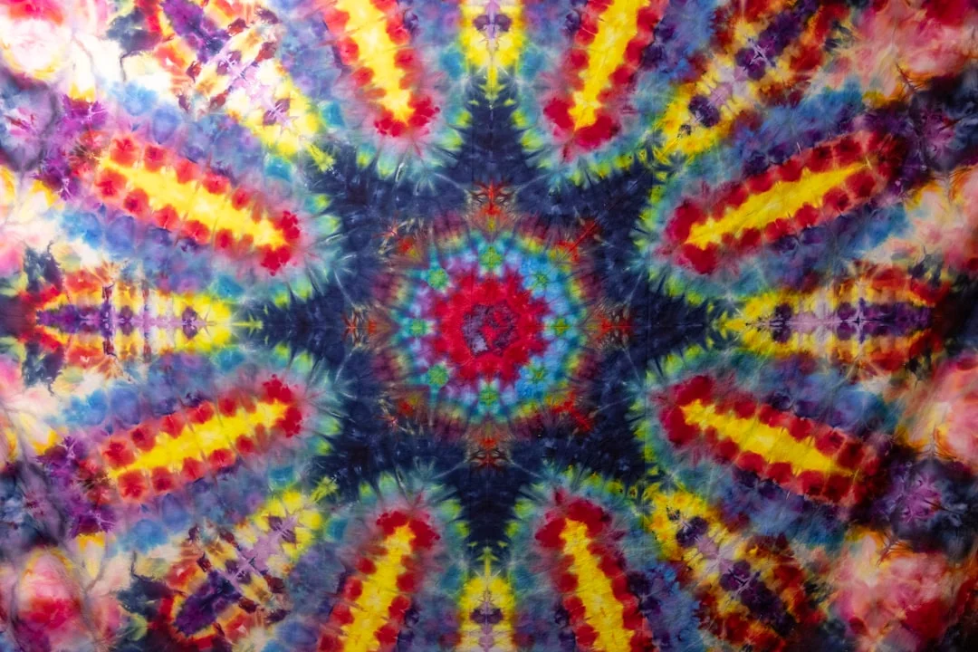 A fiber artist's studio workspace with jars of Procion MX dye powder in jewel tones, a gram scale, soda ash, and folded cotton fabric ready for dyeing